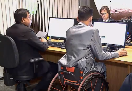 Sala de atendimento judicial do STJ com três homens no computador, um deles utiliza cadeira de rodas